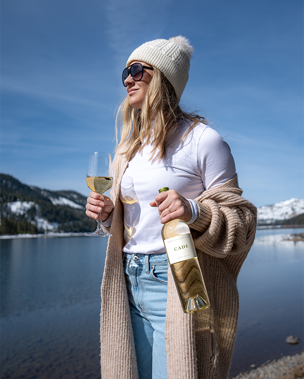 a woman holding wine glasses and standing by water