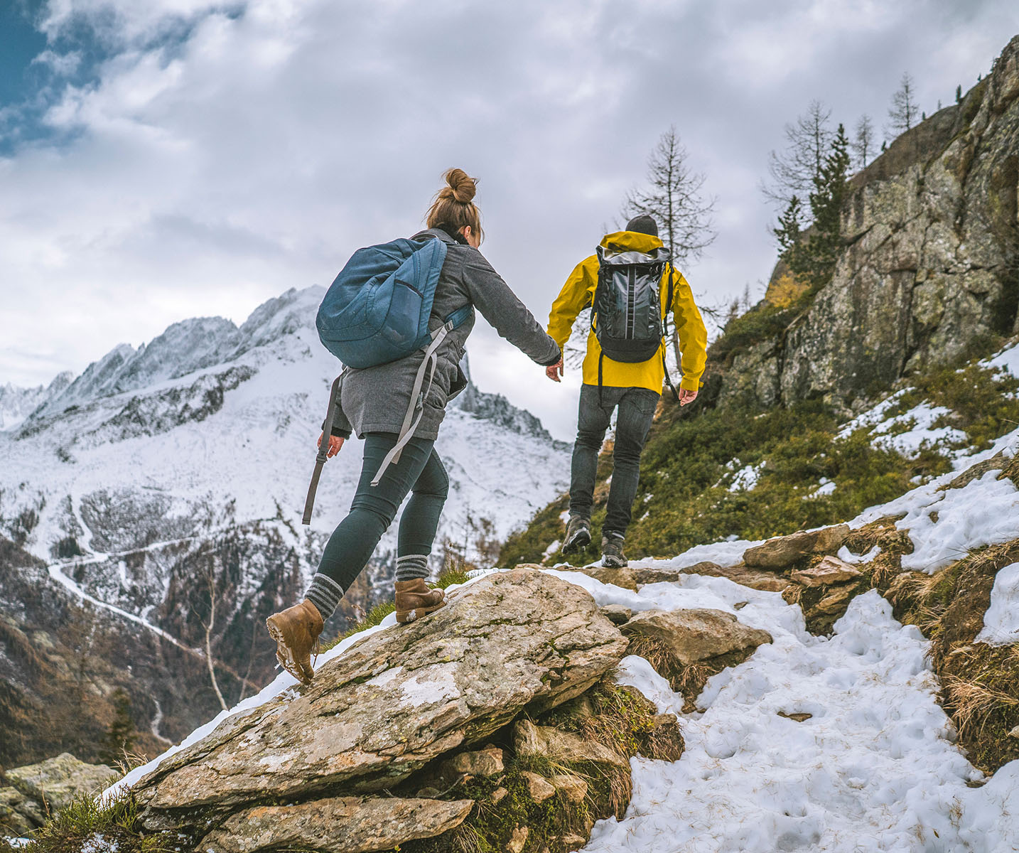 a man and woman walking on a rock with snow and mountains in the background