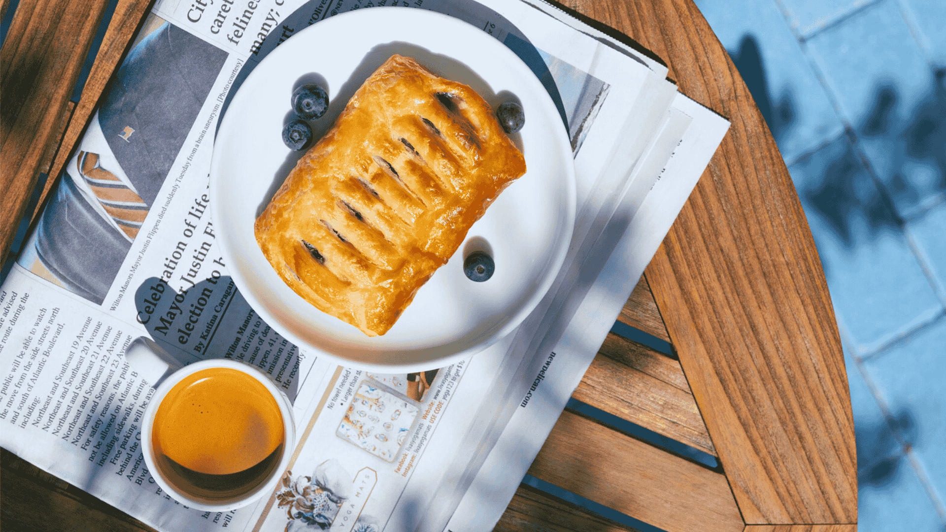 a pastry on a plate with a cup of coffee and a newspaper