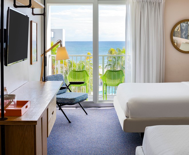 A hotel room with a double bed, desk, TV, and balcony with ocean view.