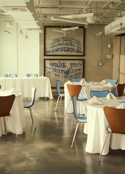 A dining room with white tablecloths, blue chairs, and large artwork on the wall.