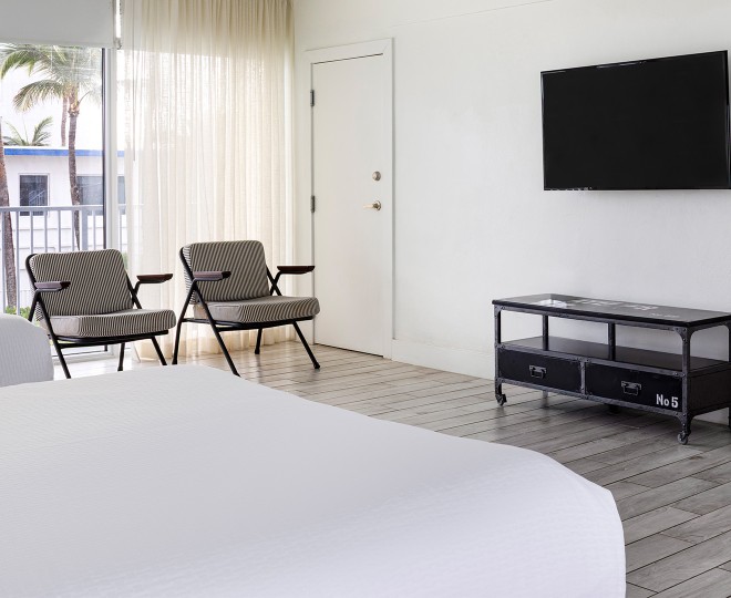 A hotel room with a bed, two chairs, a TV, and a door