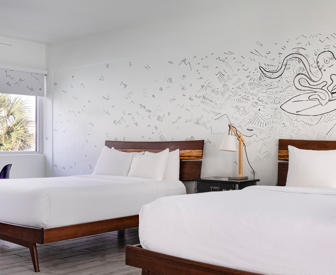 A hotel room with two twin beds, a window, and a mural of an octopus on the wall.