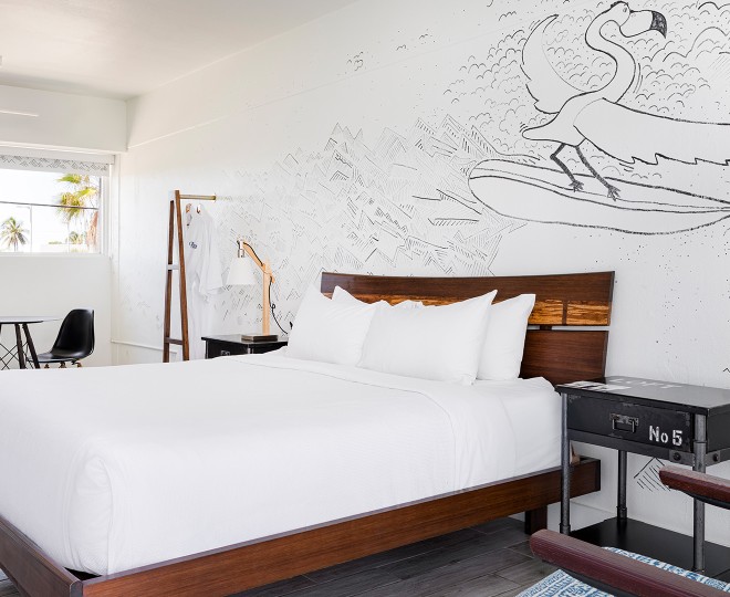 A neatly made bed with white linens and pillows in a room with a large mural on the wall.