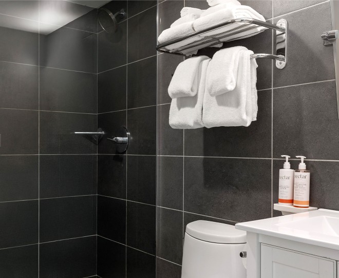 A bathroom with dark tiles, a shower, toilet, sink, and towels.