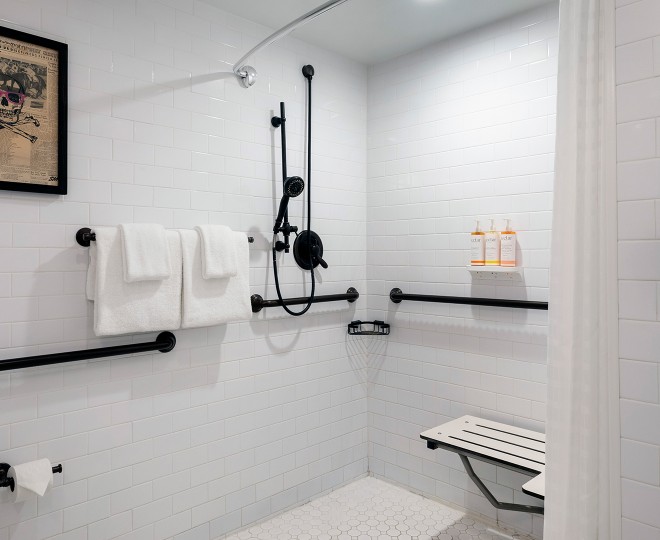 A clean and modern bathroom shower with white tiles, black fixtures, and a shower bench.