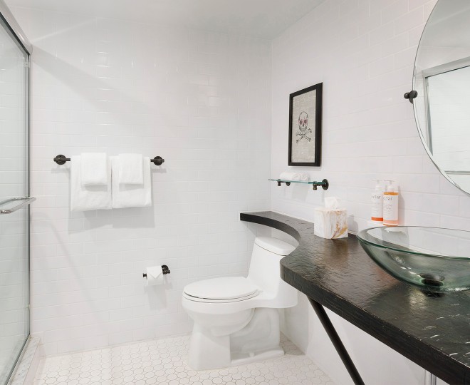 A clean and modern bathroom with white tiles, a glass sink, and a toilet.