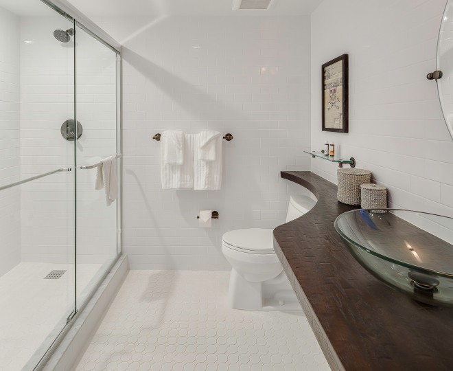A clean bathroom with a glass-enclosed shower, white tile, and a dark wood countertop with a glass sink bowl.