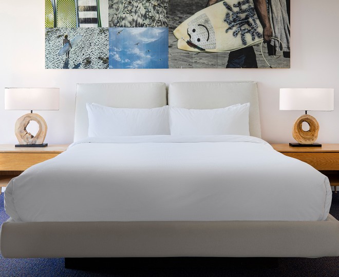 A neatly made bed with white linens and a large piece of artwork above it.