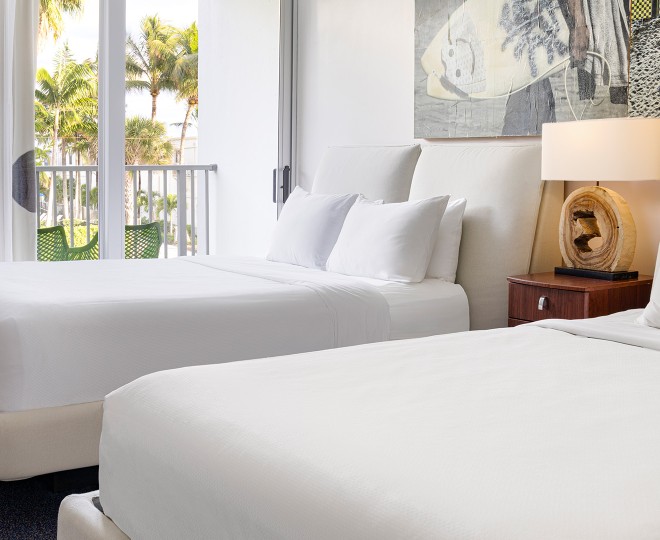 A bright room with two beds, a balcony, and a view of palm trees.