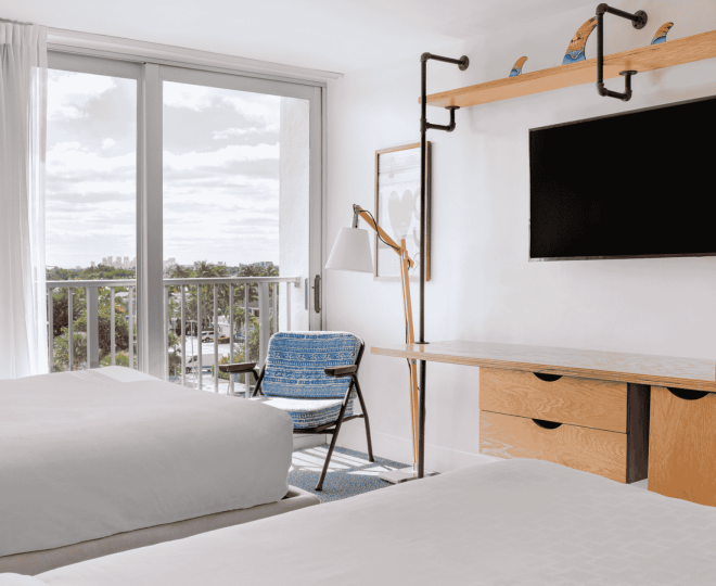 A hotel room with a balcony, two beds, a desk, and a TV.