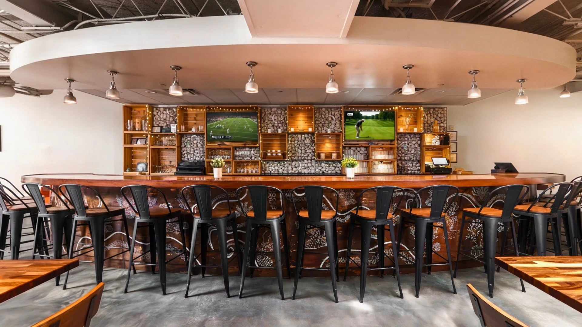 A long bar with stools and TVs on the wall