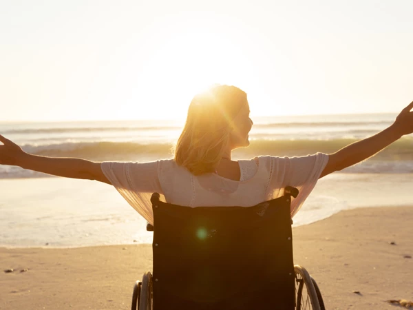 woman in a wheelchair open her arms on the beach