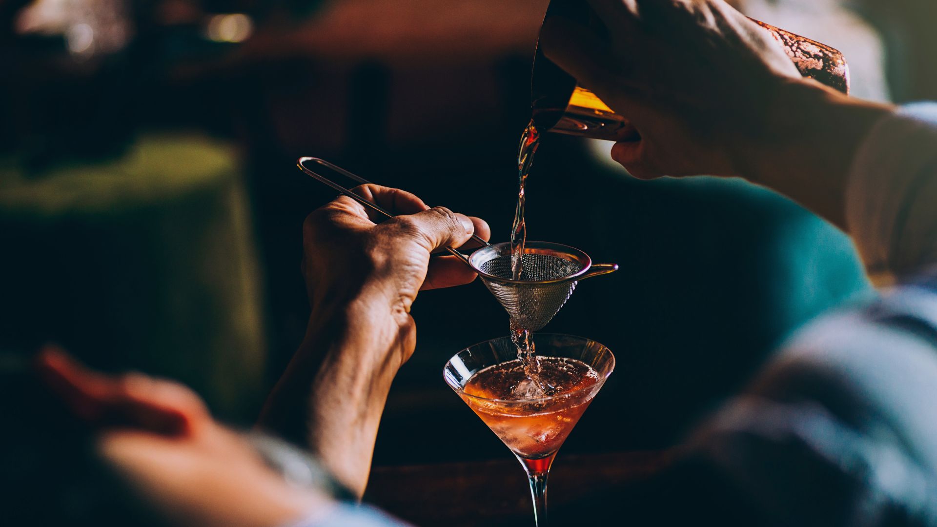 a person pouring liquid into a martini glass