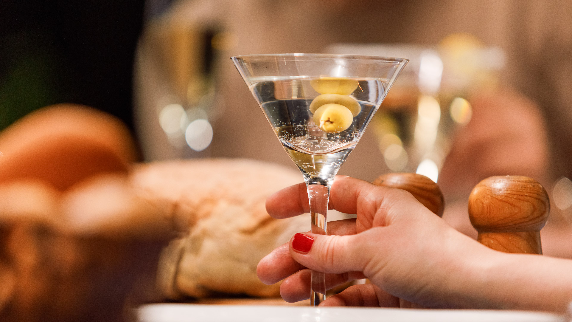 a hand holding a martini glass with olives in it