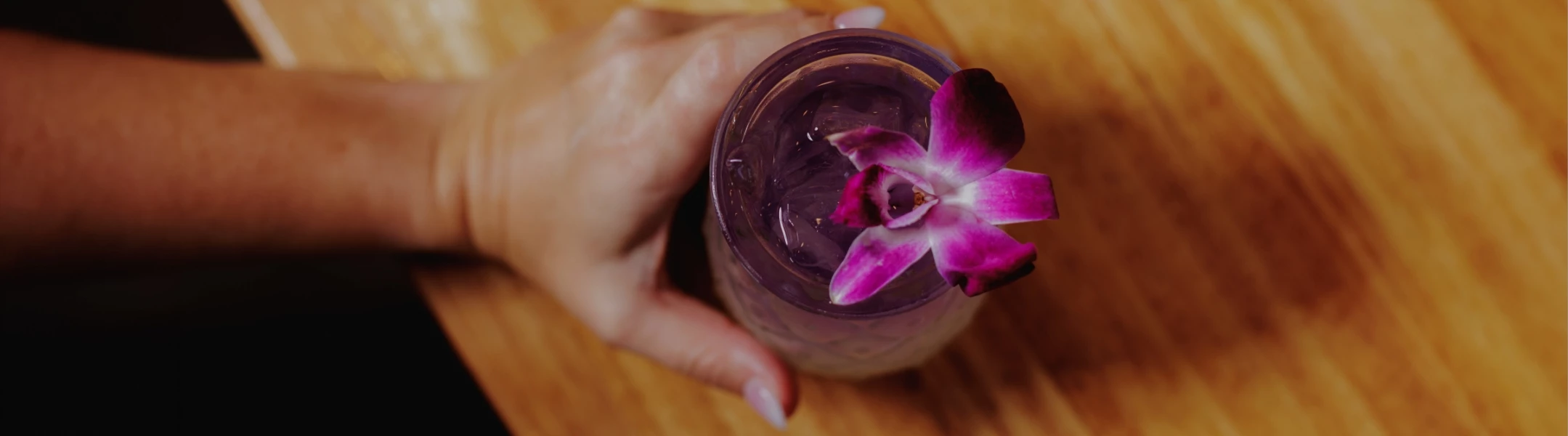 a hand holding a glass with a purple flower on top