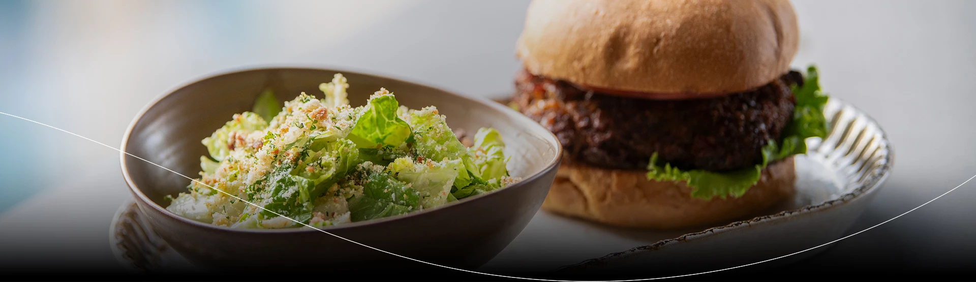 a bowl of salad next to a burger