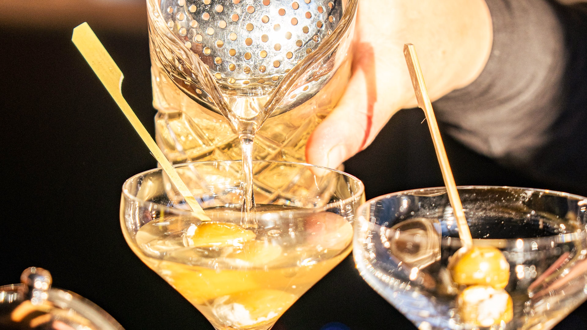a person pouring a drink into a martini glass