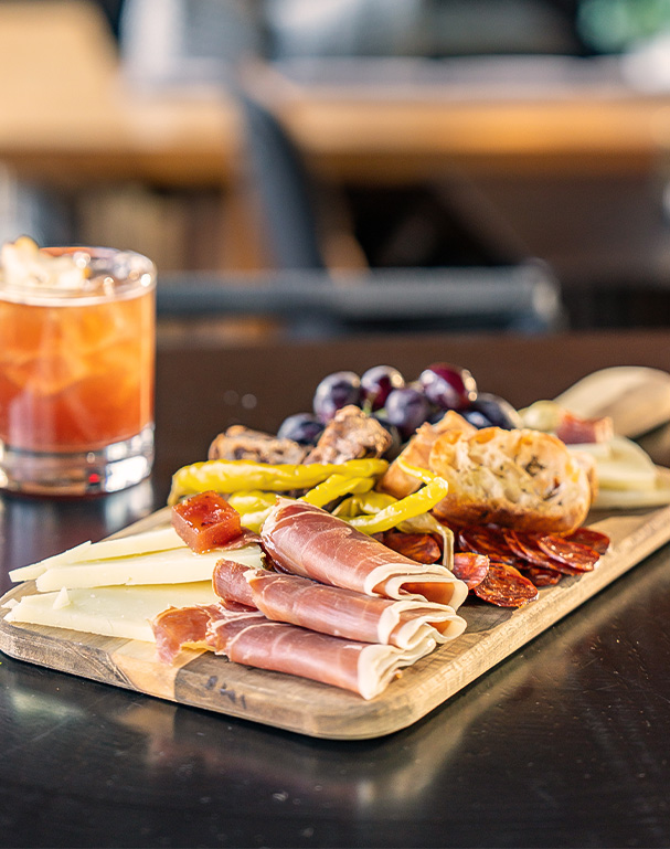 a board with meat and cheese and grapes on a table previus