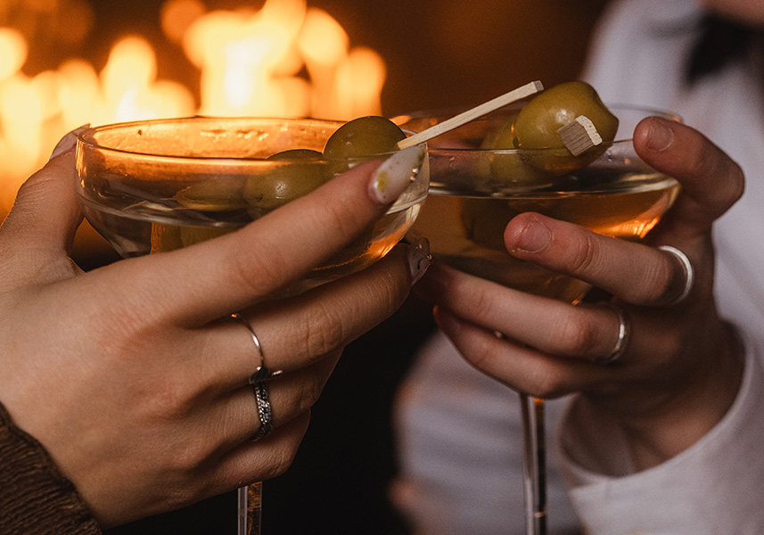 a pair of hands holding a martini glass with olives