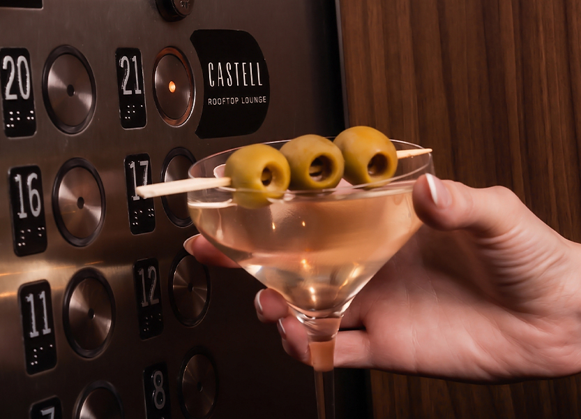 a hand holding a martini glass with olives on top