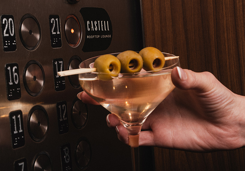 a hand holding a martini glass with olives on it