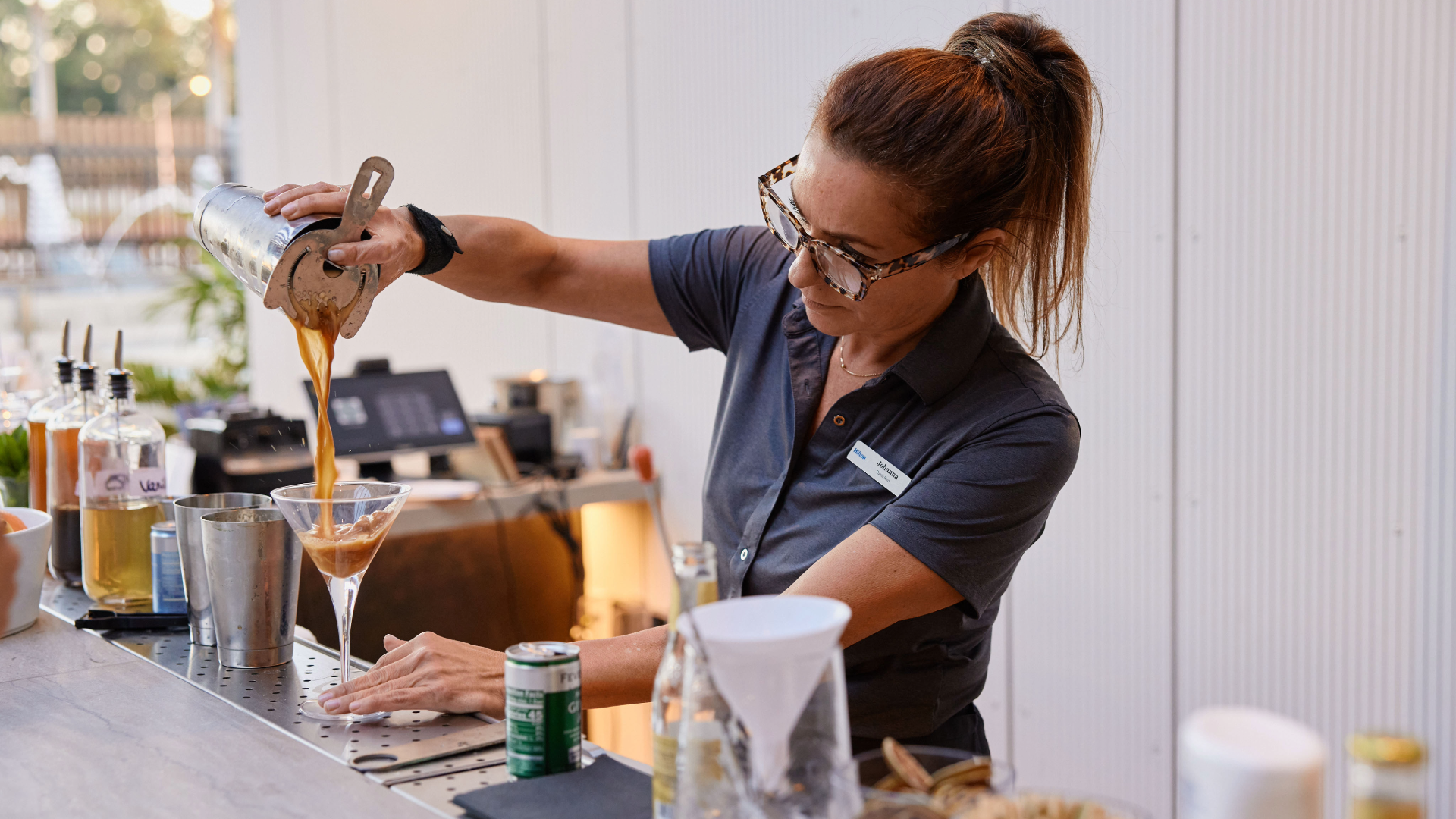a woman pouring brown liquid into a martini glass