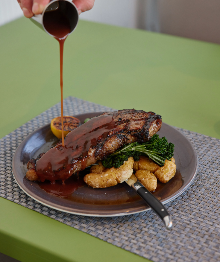 a plate of steak and vegetables with sauce being poured onto it
