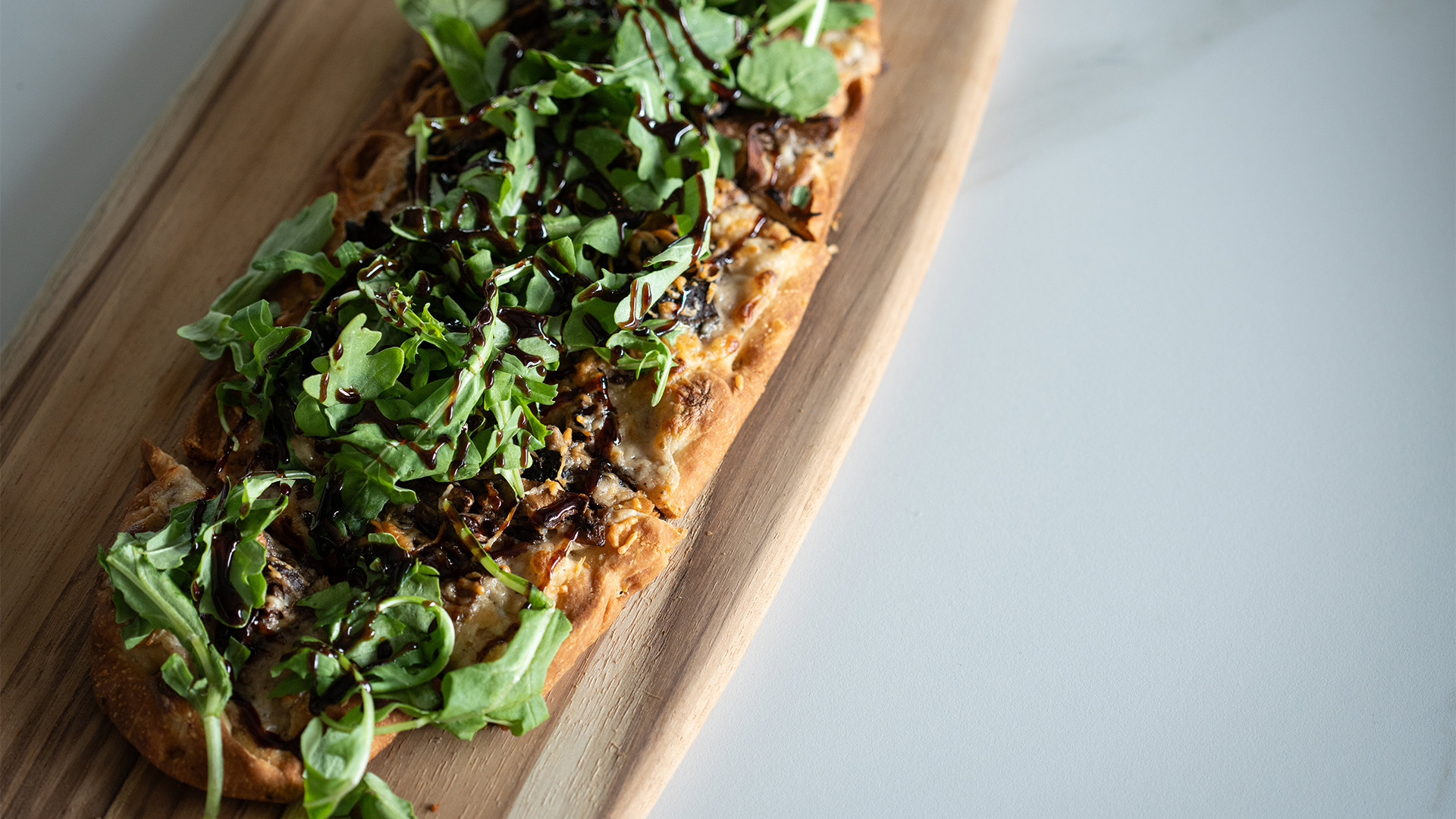 a long pizza with greens on it