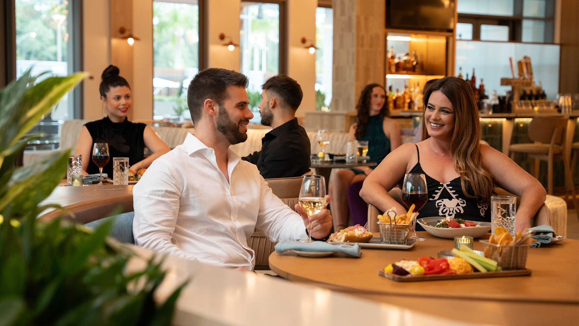 a man and woman sitting at a table with food and drinks