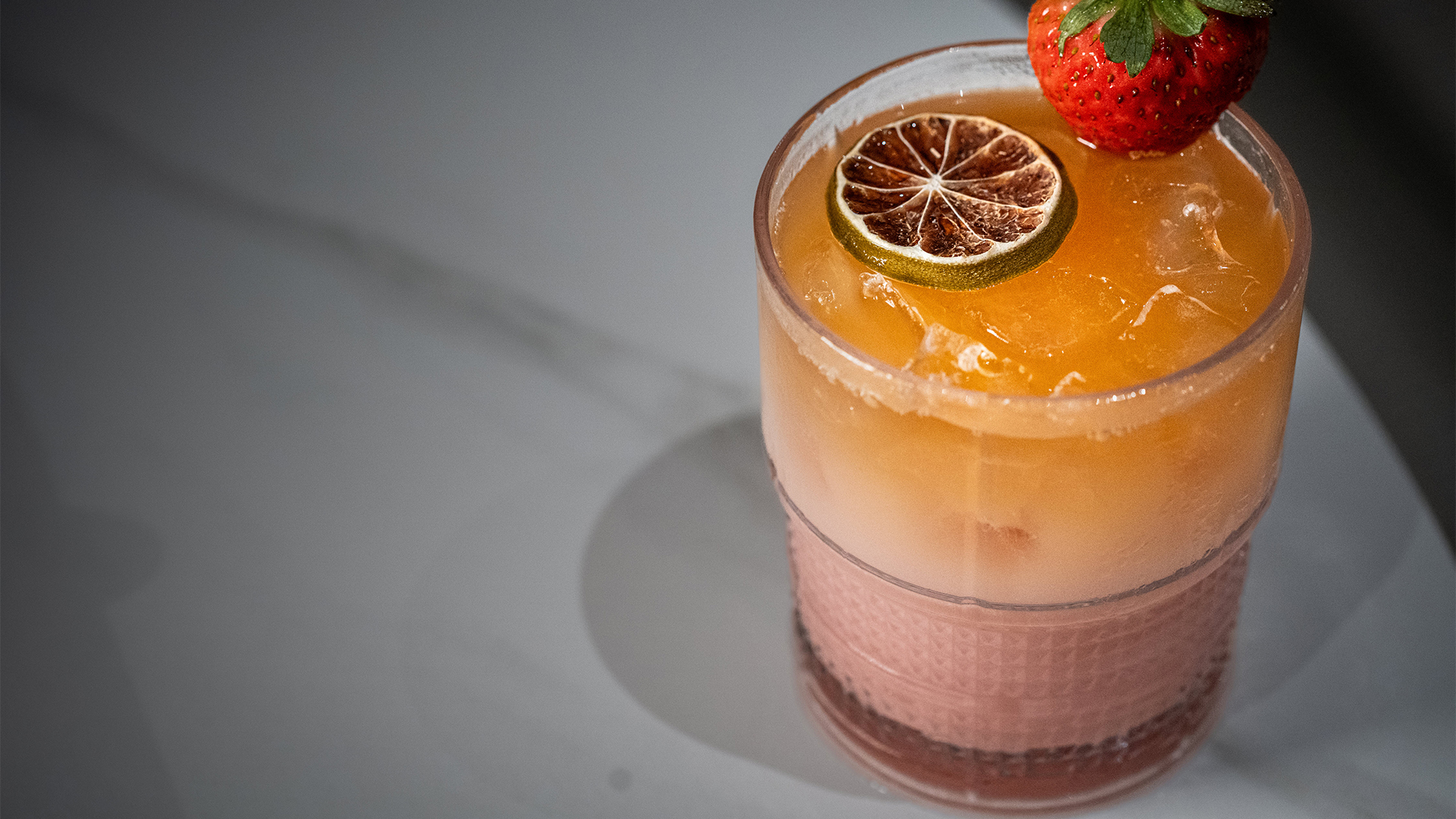 a glass with a drink and a slice of lime and a strawberries on top