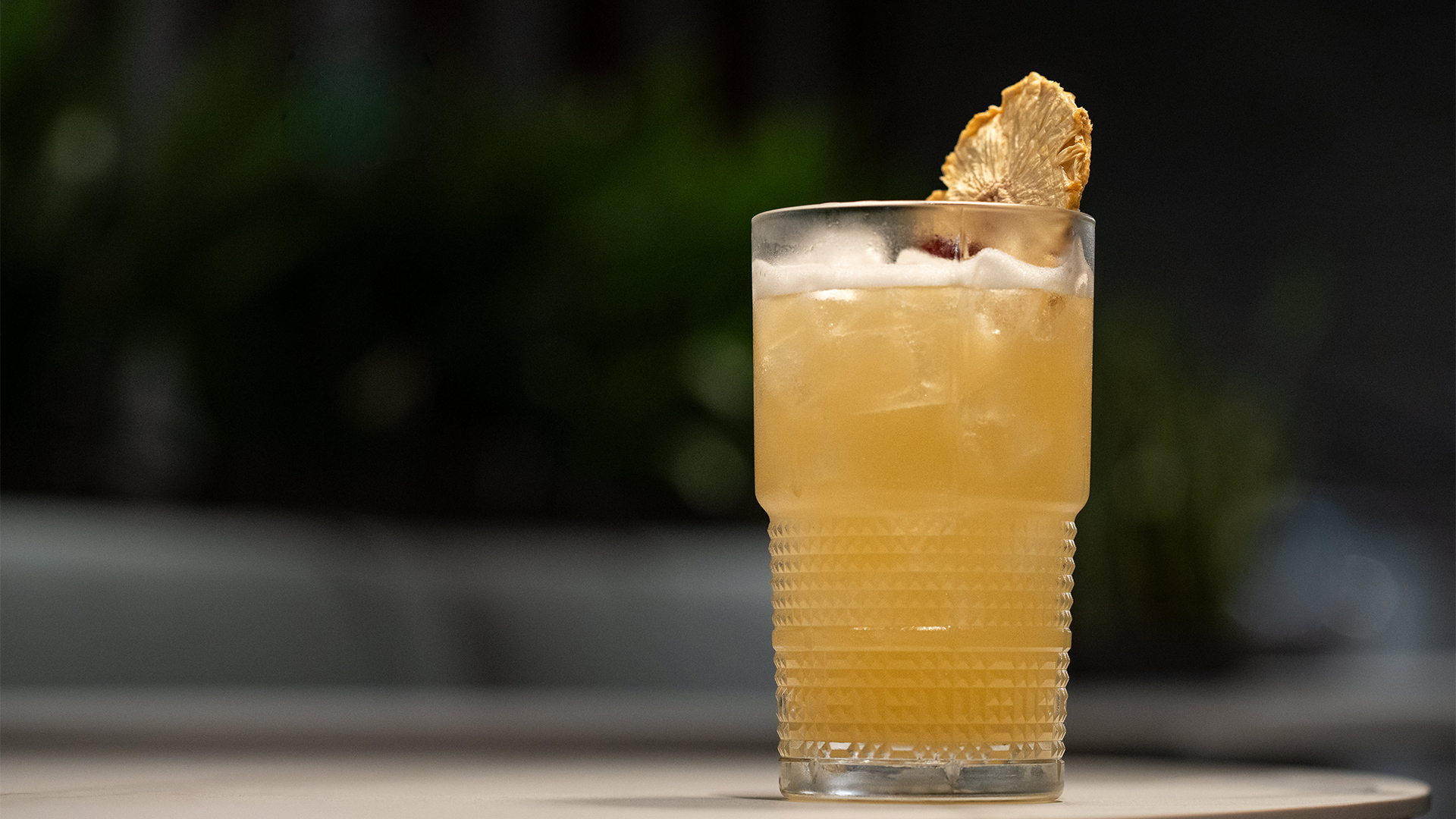 a glass of yellow liquid with a slice of pineapple on top