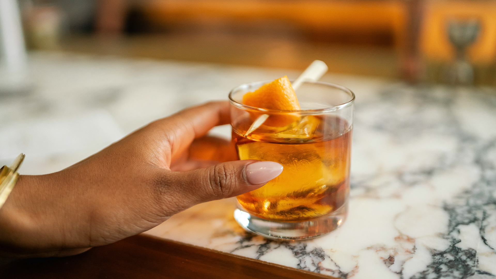 a hand holding a glass of liquid with an orange slice
