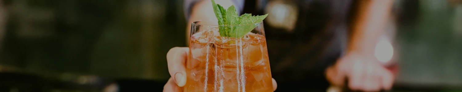 a hand holding a glass of liquid with a leafy green leaf