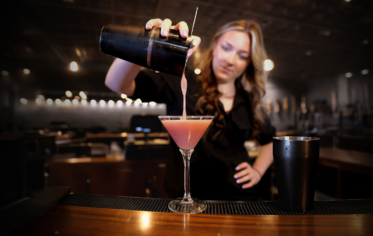 a woman pouring a drink into a martini glass