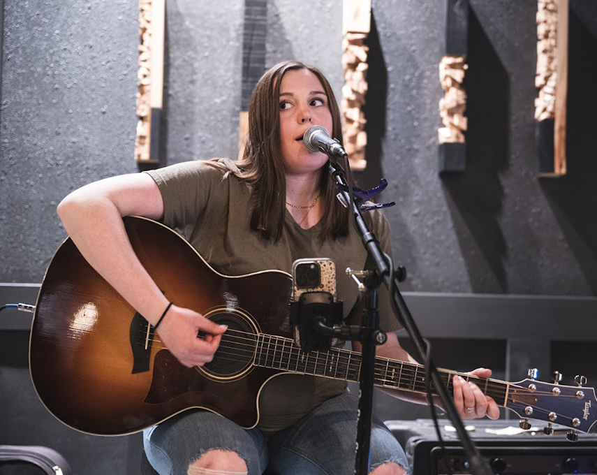 a woman playing guitar and singing into a microphone