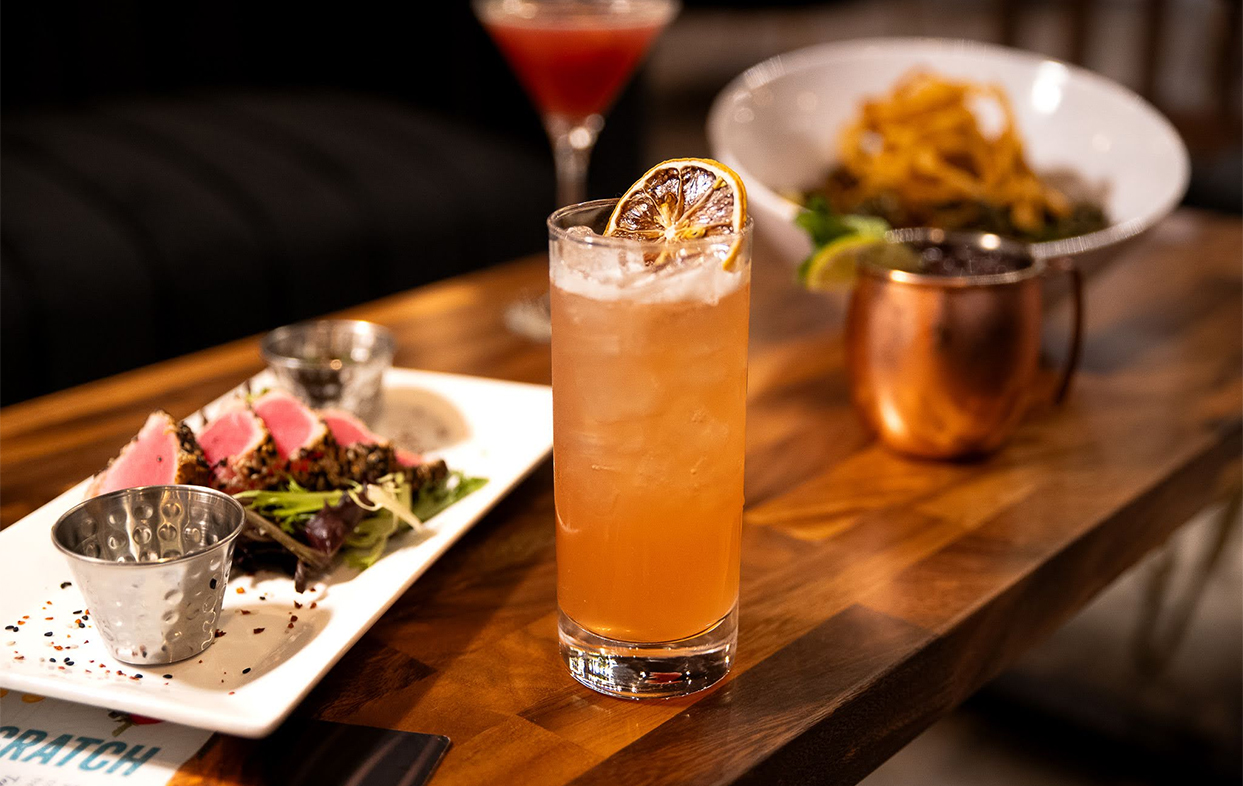a glass of liquid with a slice of orange on top of a table with food