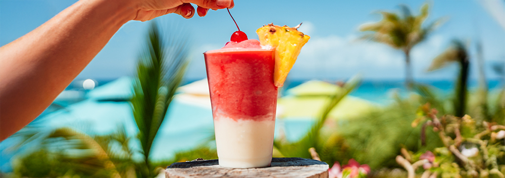 a hand holding a cherry in a glass with a red and white drink