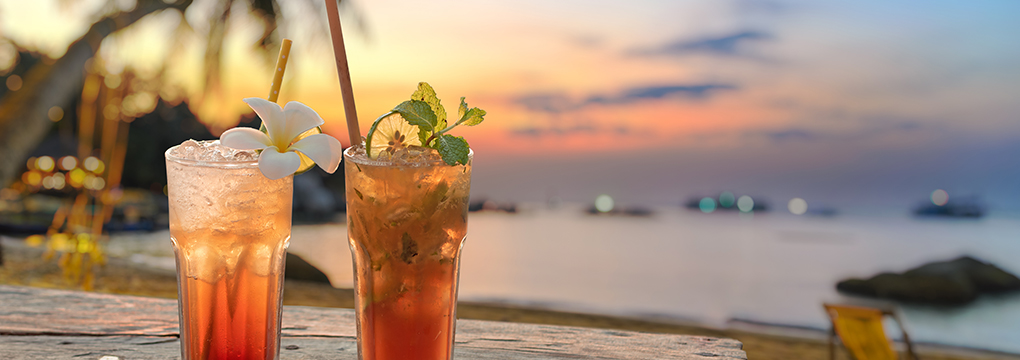 a glass of liquid with a straw and a straw in front of a beach