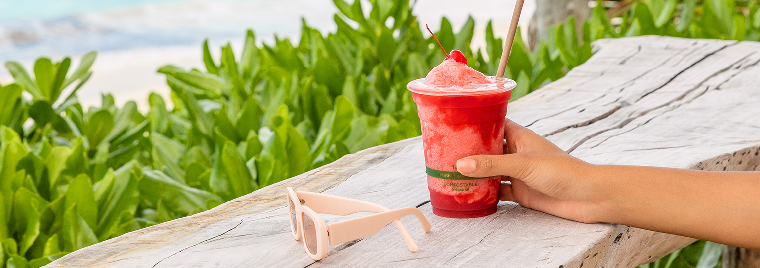 a hand holding a cup of red liquid with a cherry on top