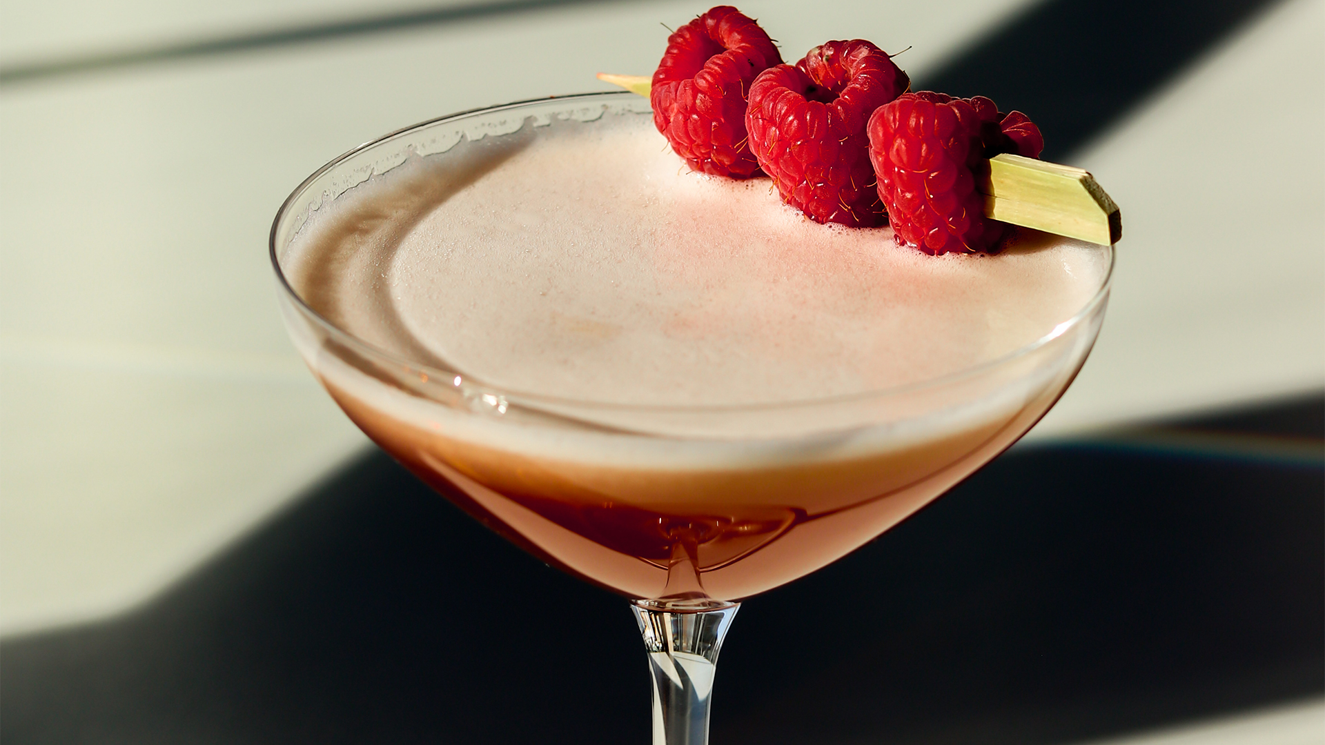a glass with a drink and raspberries on it