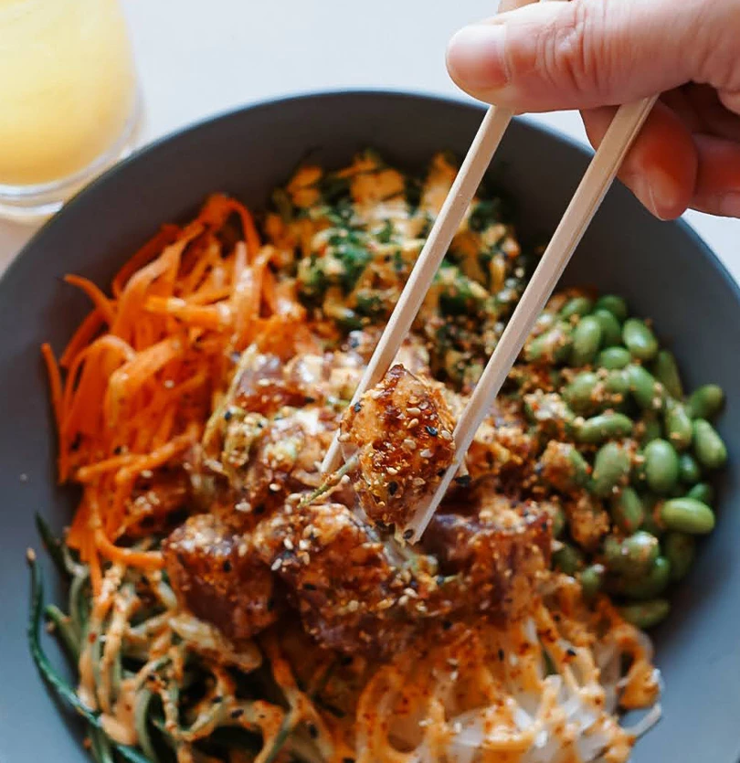 a person holding chopsticks to a bowl of food