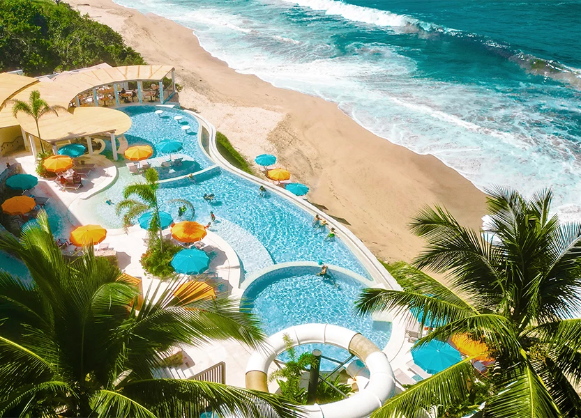 a swimming pool with umbrellas and palm trees on a beach
