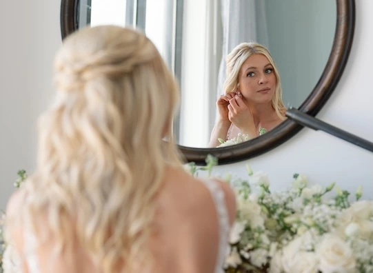 a woman looking at her earrings in a mirror