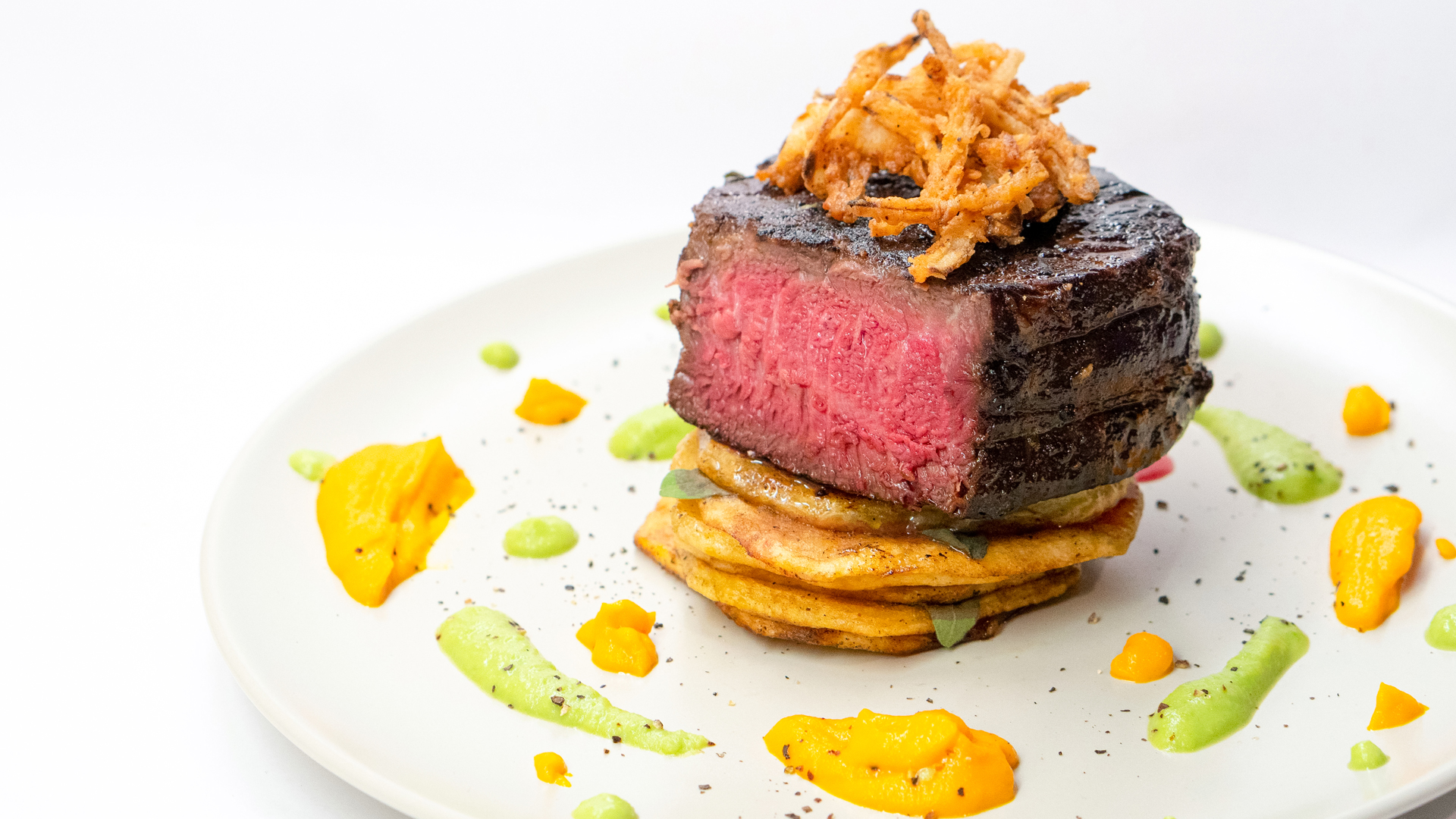 Medium-rare steak with crispy topping and sauces on a plated dish
