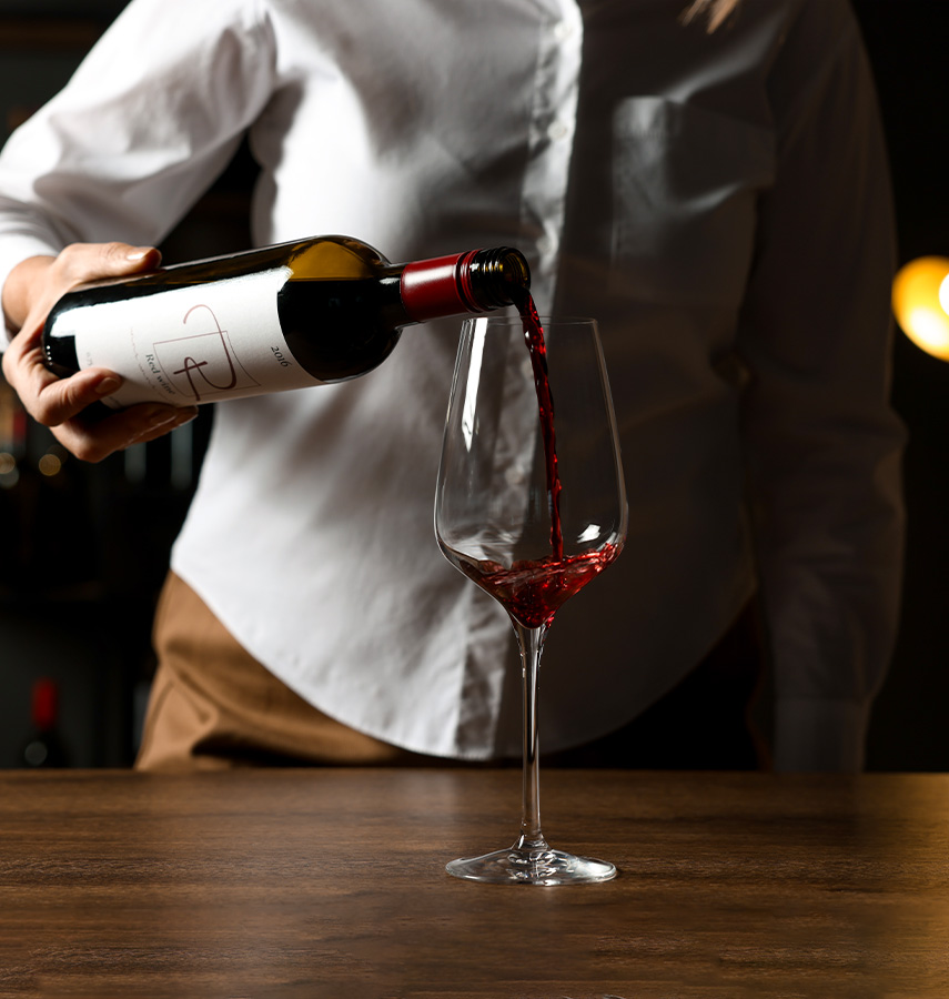 a person in a white button down pouring red wine into a glass on a wooden table