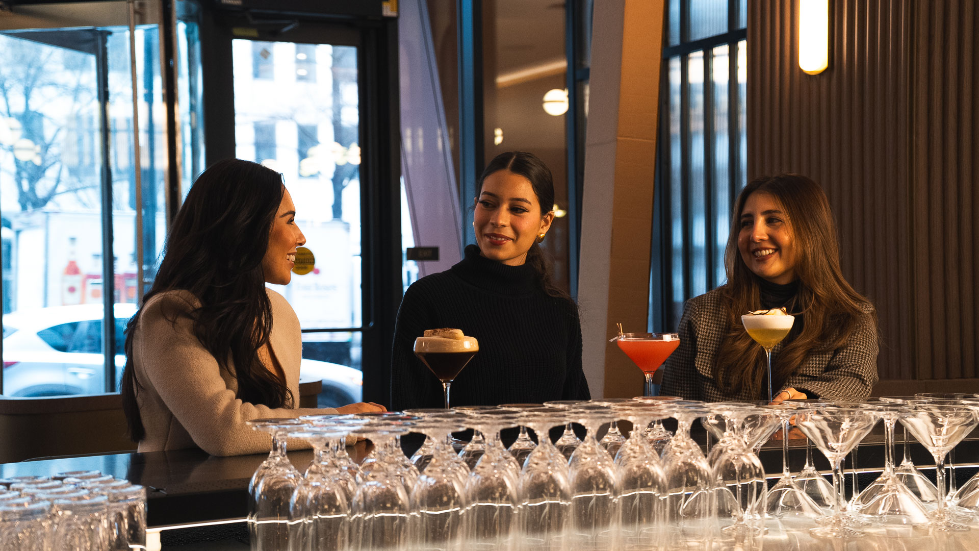 a group of women sitting at a bar with glasses of wine