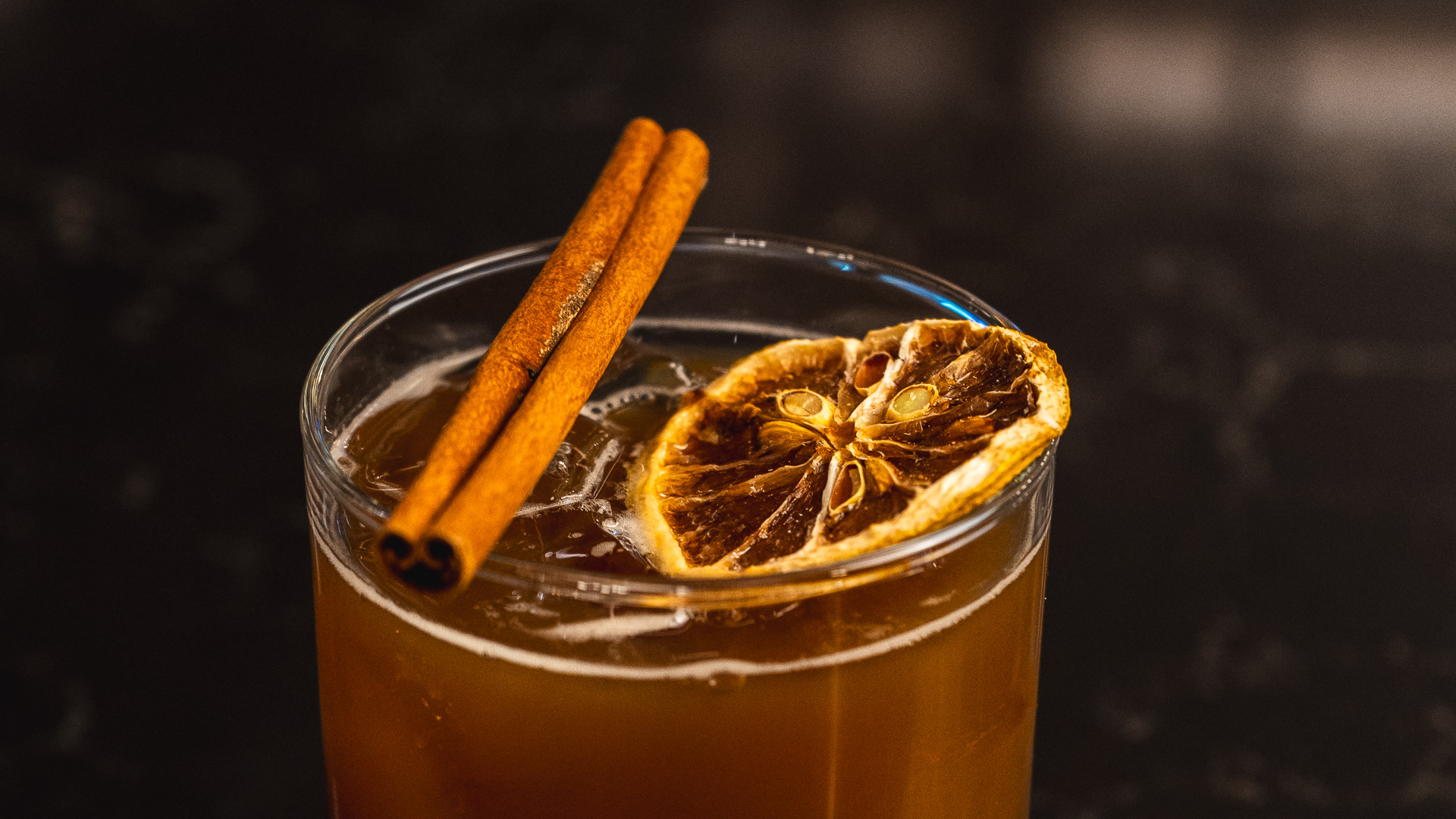 a glass of liquid with a slice of orange and cinnamon sticks