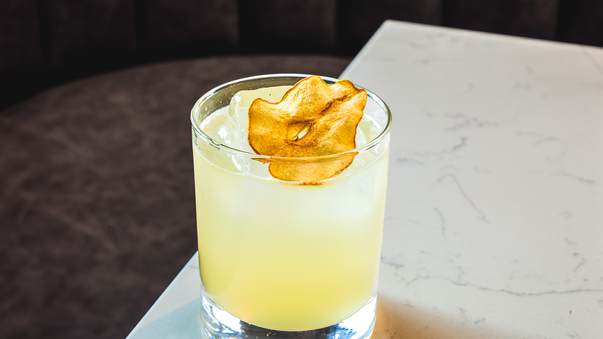 a glass of yellow liquid with a chip on top