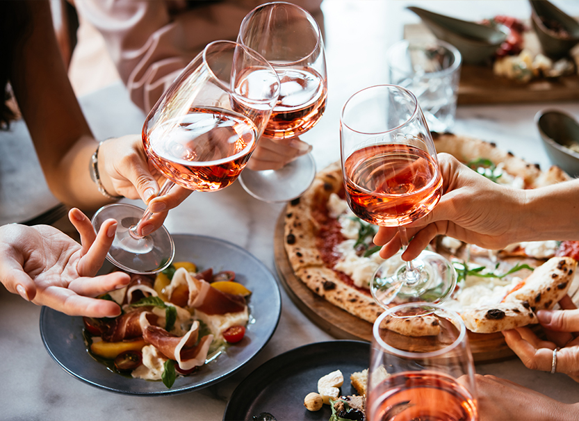 a group of people holding wine glasses and eating pizza